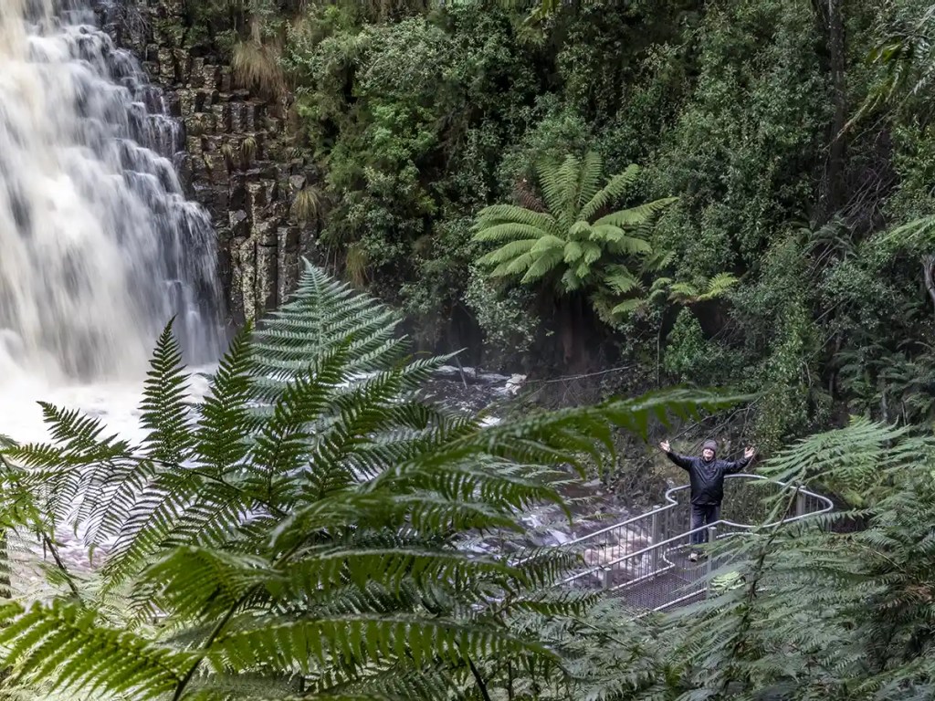 Graham is standing on a platform at the base of a gushing waterfall in North West Tasmania.